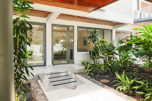 A modern building with a covered entrance, glass doors, and a garden area with various plants.