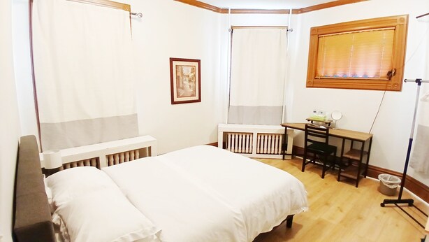 Een slaapkamer met een bed, een bureau, een radiator, een raam met zonwering en een foto aan de muur.