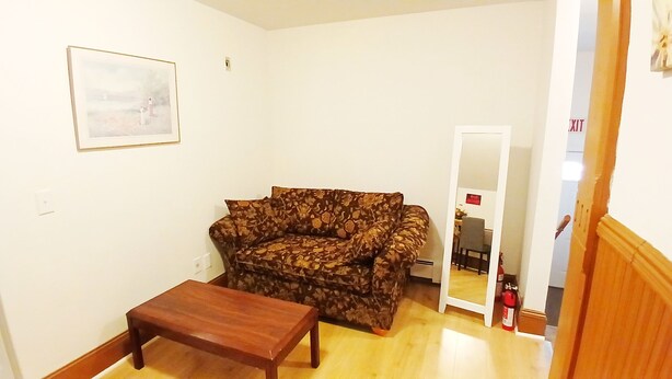 A living room with a floral sofa, a wooden coffee table, a framed picture on the wall, and a door leading to another room. - Cozy spacious bedroom with king size bed, only half mile to Rt.95, private bath (New London)