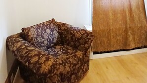 Een kamer met een houten vloer, een bank met bloemenprint, een airconditioning en een gordijn.