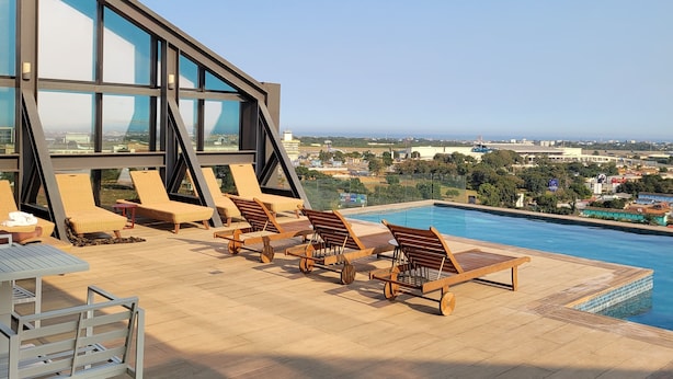 A rooftop pool area with sun loungers and a table, overlooking a cityscape. - RT PROPERTIES AT KASS TOWERS  (Accra)