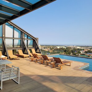 A rooftop pool area with sun loungers and a table, overlooking a cityscape. - RT PROPERTIES AT KASS TOWERS (Accra)