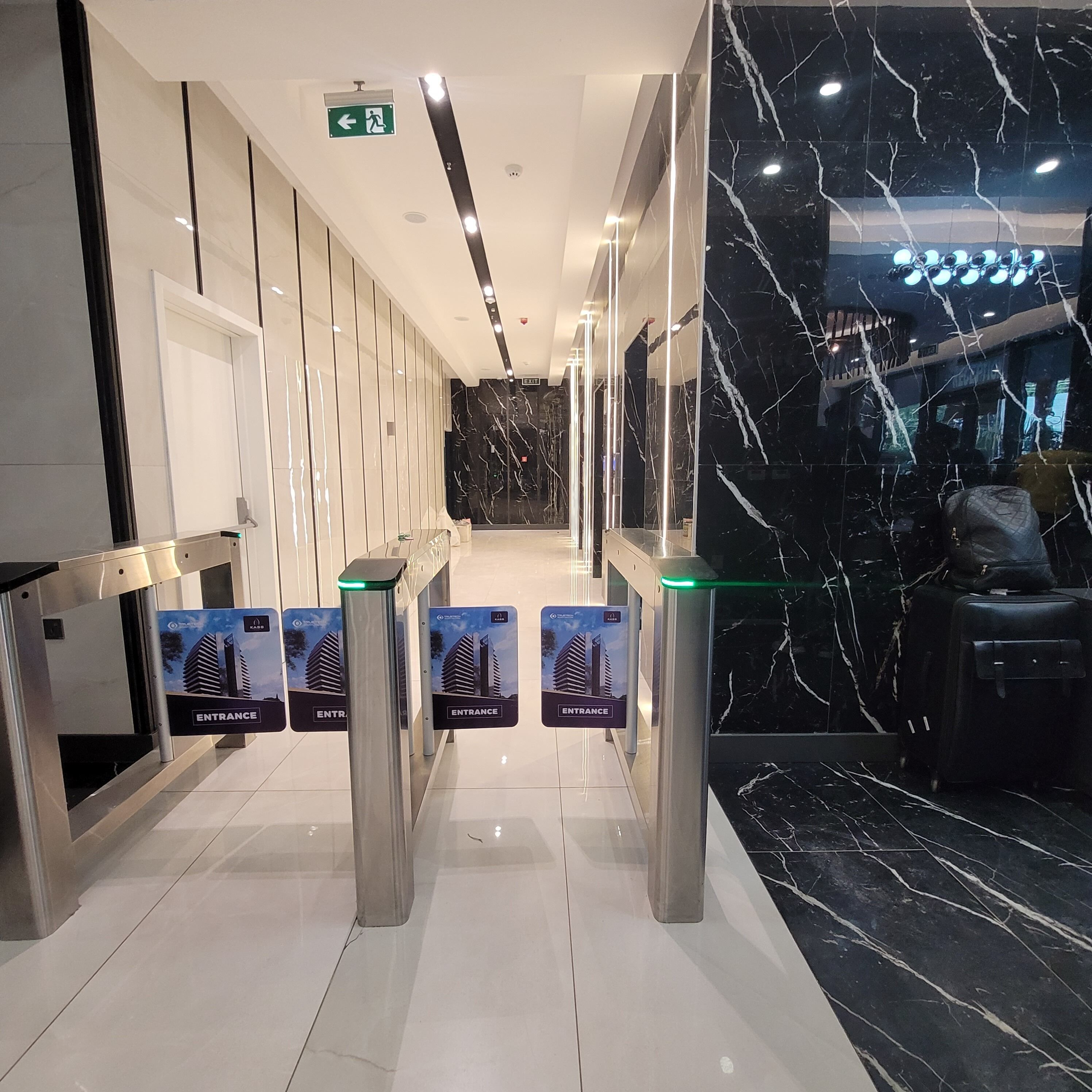 A modern hotel lobby with a marble reception desk, a glass partition, and a clear exit sign.