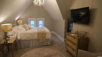 A bedroom with a bed, bedside lamps, a dresser, a television, and a chandelier.