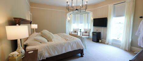 A bedroom with a large bed, bedside lamps, a TV, and a window with curtains.