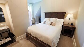 A neatly arranged bedroom with a large bed, a bedside table with a lamp, a small cabinet, and a mirror.