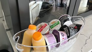 A glass container on a counter with various food items, including bottles and containers of cottage cheese, yogurt, and other dairy products. - Mon Bijou (Oconomowoc)