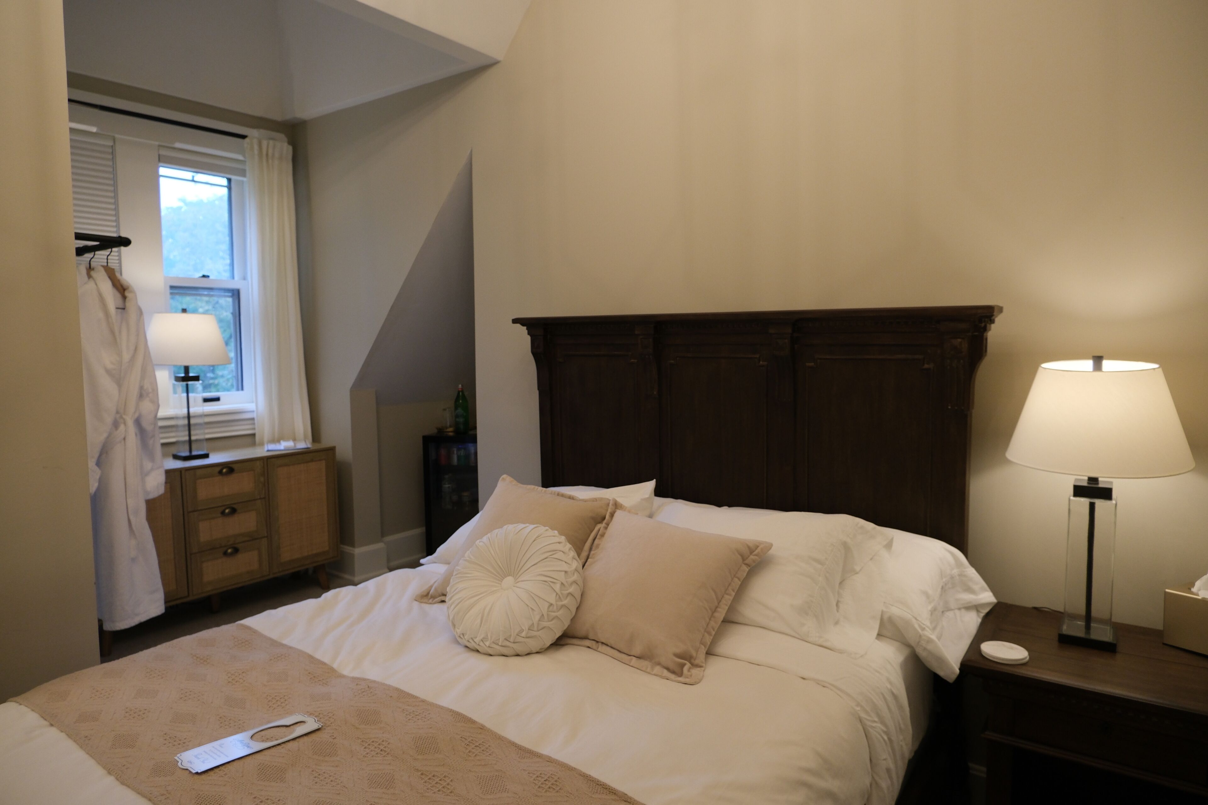 A neatly made bed with a remote control, a bedside lamp, and a wooden nightstand.