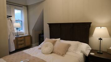 A neatly made bed with a remote control, a bedside lamp, and a wooden nightstand.