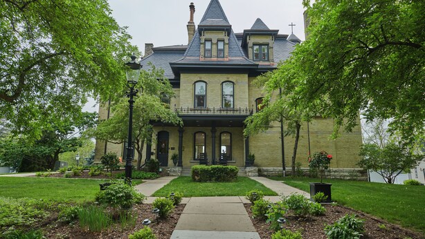 A Victorian-style house with a prominent front entrance, a steeply pitched roof, and a brick facade. - Mon Bijou (Oconomowoc)