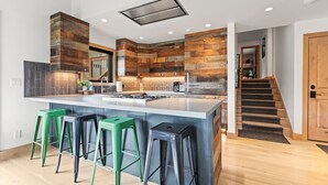 Une cuisine moderne dotée d’un grand îlot central, de tabourets de bar verts et d’un mur d’accent en bois.