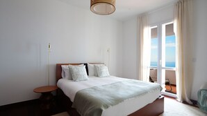Een slaapkamer met een bed, nachtkastjes, uitzicht op zee en een balkon.
