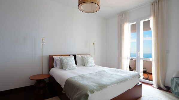 Een slaapkamer met een bed, nachtkastjes, uitzicht op zee en een balkon.