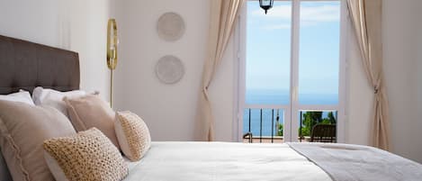 A bedroom with a large bed, a view of the sea through a balcony, and a hanging lantern.