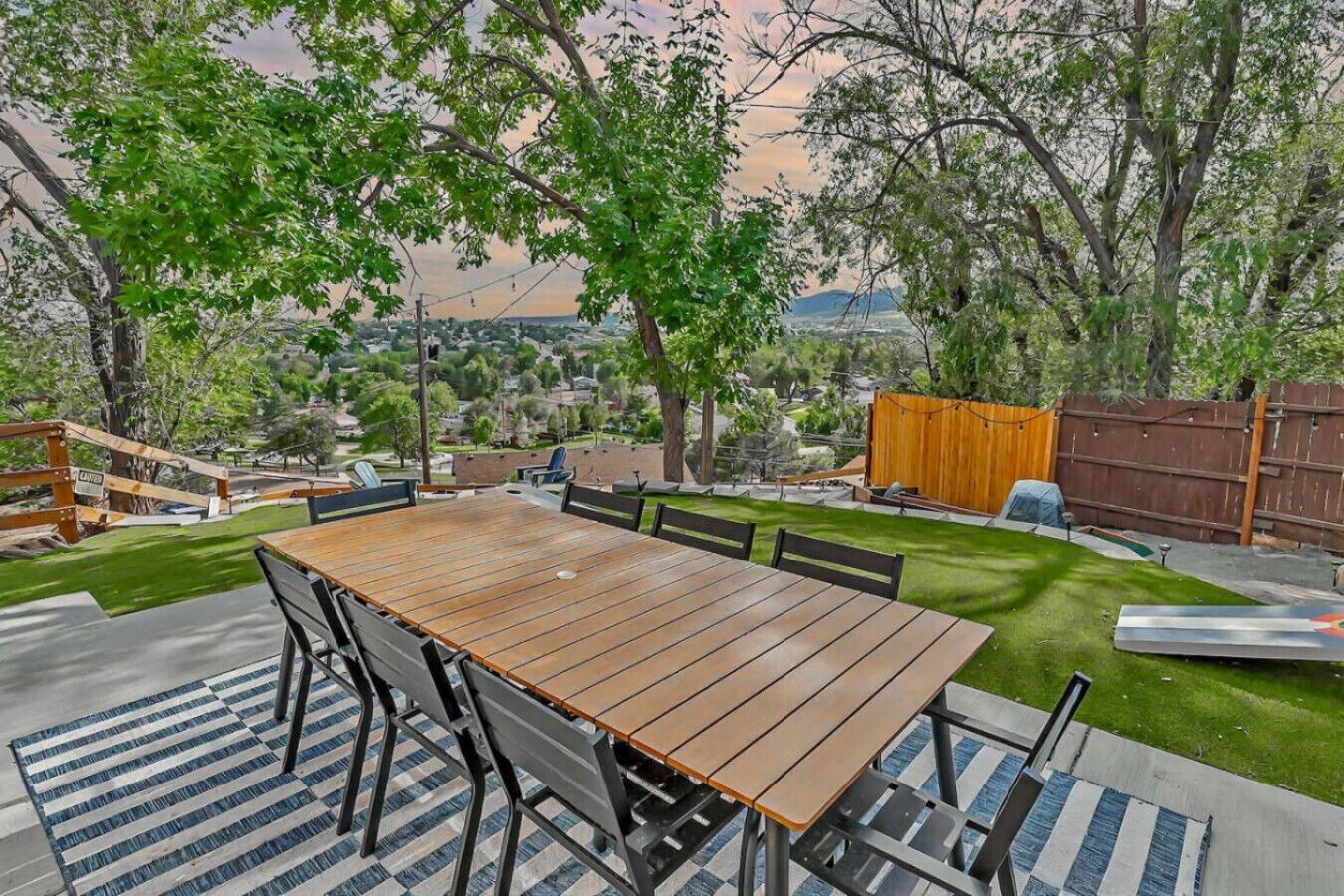 A backyard with a wooden table and chairs, a barbecue grill, and a wooden fence.