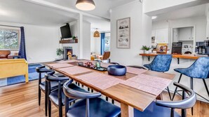 A modern dining area with a long wooden table, blue chairs, and pendant lighting. - Mountain Views ~Climbing wall ~Mini Golf ~Hot tub (Colorado Springs)