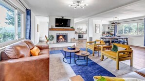 A spacious living room with a fireplace, a dining area, and a kitchen. - Mountain Views ~Climbing wall ~Mini Golf ~Hot tub (Colorado Springs)