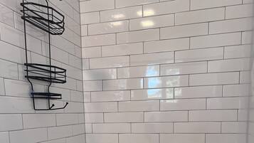 A shower area with white subway tiles, a chrome showerhead, and a black towel rack.