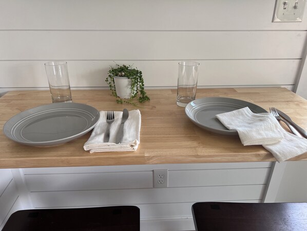 A neatly set dining table with two plates, cutlery, and glasses, a small potted plant, and a white napkin on a wooden table.