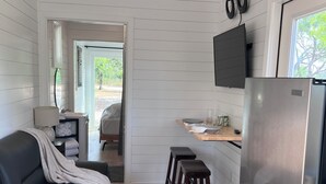 Uma cozinha compacta com geladeira embutida, banquetas de madeira, uma mesa de jantar e uma TV fixada na parede.