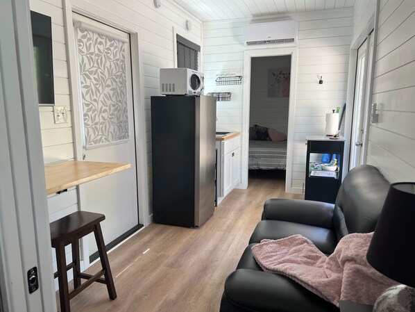 A compact living space with a kitchenette, a bed, a seating area with a blanket, and a small table.