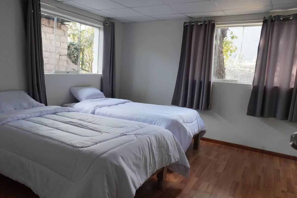 Una habitación con dos camas, cortinas grises y suelo de madera.
