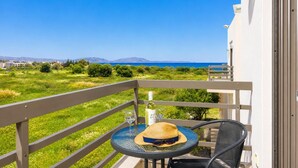 Un balcon avec une table, un chapeau et une bouteille de vin, d’où l’on peut admirer un paysage verdoyant et la mer.