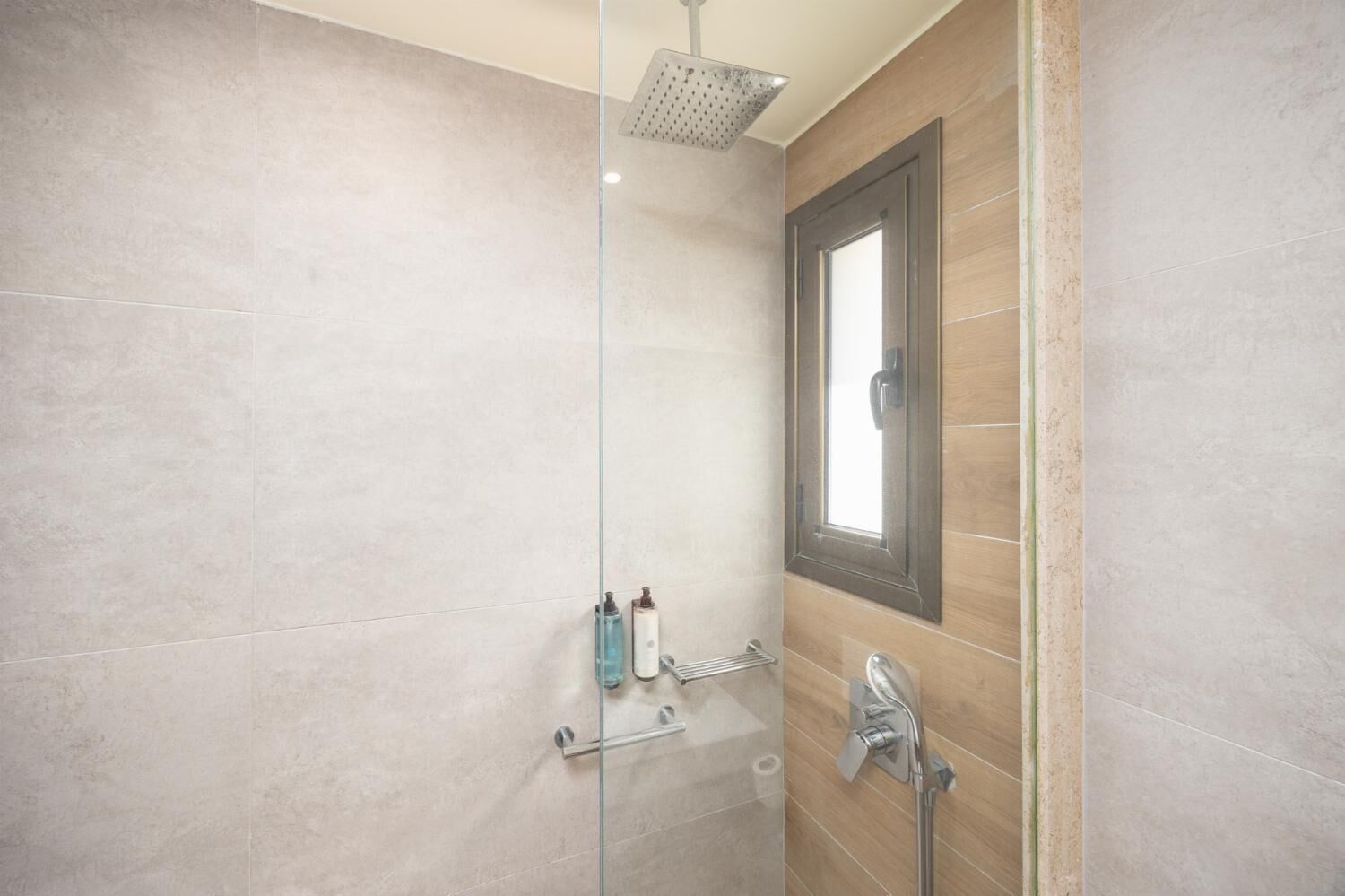 A modern shower with a glass door, a window, and a towel rack.