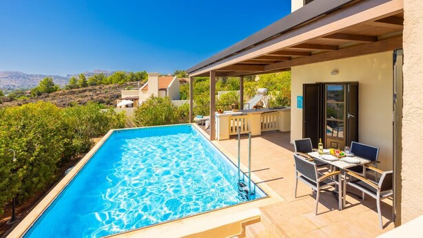 Ein Schwimmbecken mit überdachter Terrasse, Gartenmöbeln und Blick auf die umliegende Landschaft.