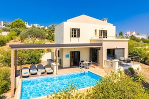 Une maison moderne à deux étages, dotée d’une piscine, d’un espace de détente extérieur et offrant une vue sur le paysage environnant.