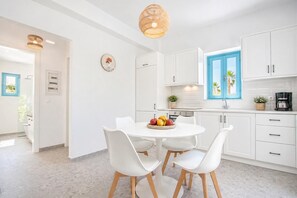 A modern kitchen with white cabinets, a round dining table with white chairs, and a fruit bowl.