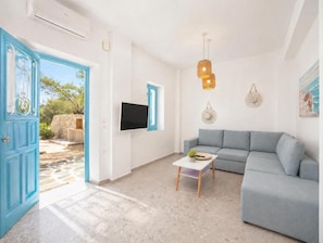 A living room with a grey sofa, a small coffee table, a TV mounted on the wall, and a blue door leading outside.