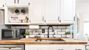 A kitchen with white cabinets, a black microwave, a sink, and a wooden countertop. - Serenity WR Deluxe Escape Indoor Pool (Warner Robins)