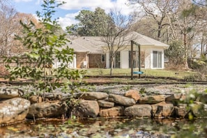 A house with a stone wall in the foreground, a grassy yard, and a clear sky.