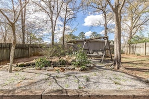A backyard with a wooden structure, trees, and a gravel area.