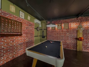 A billiards table in a room with brick walls, a dartboard, and a clock.
