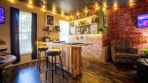 A bar area with stools, a counter, and a brick wall with a television. - Serenity WR Deluxe Escape Indoor Pool (Warner Robins)