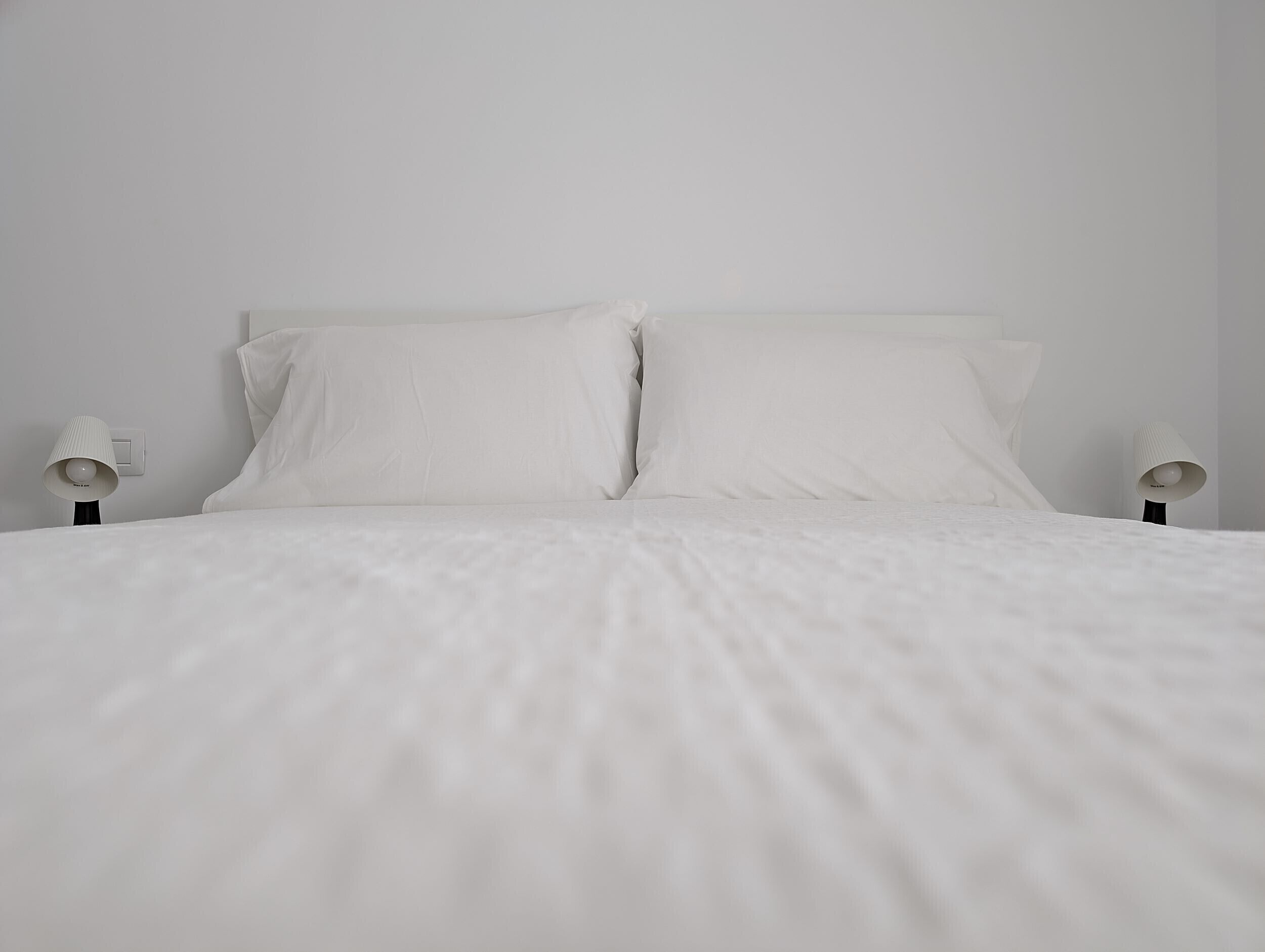 Ein ordentlich bezogenes Bett mit weißer Bettwäsche und zwei Nachttischlampen.