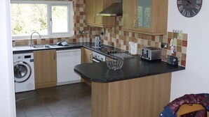 Cocina compacta con lavavajillas integrado, un lavamanos y una estufa. Hay un reloj en la pared y una ventana que proporciona luz natural.