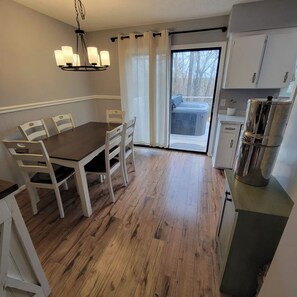 A dining area with a table and chairs, a chandelier, a sliding glass door leading to a balcony, and a kitchenette with cabinets and a stove.