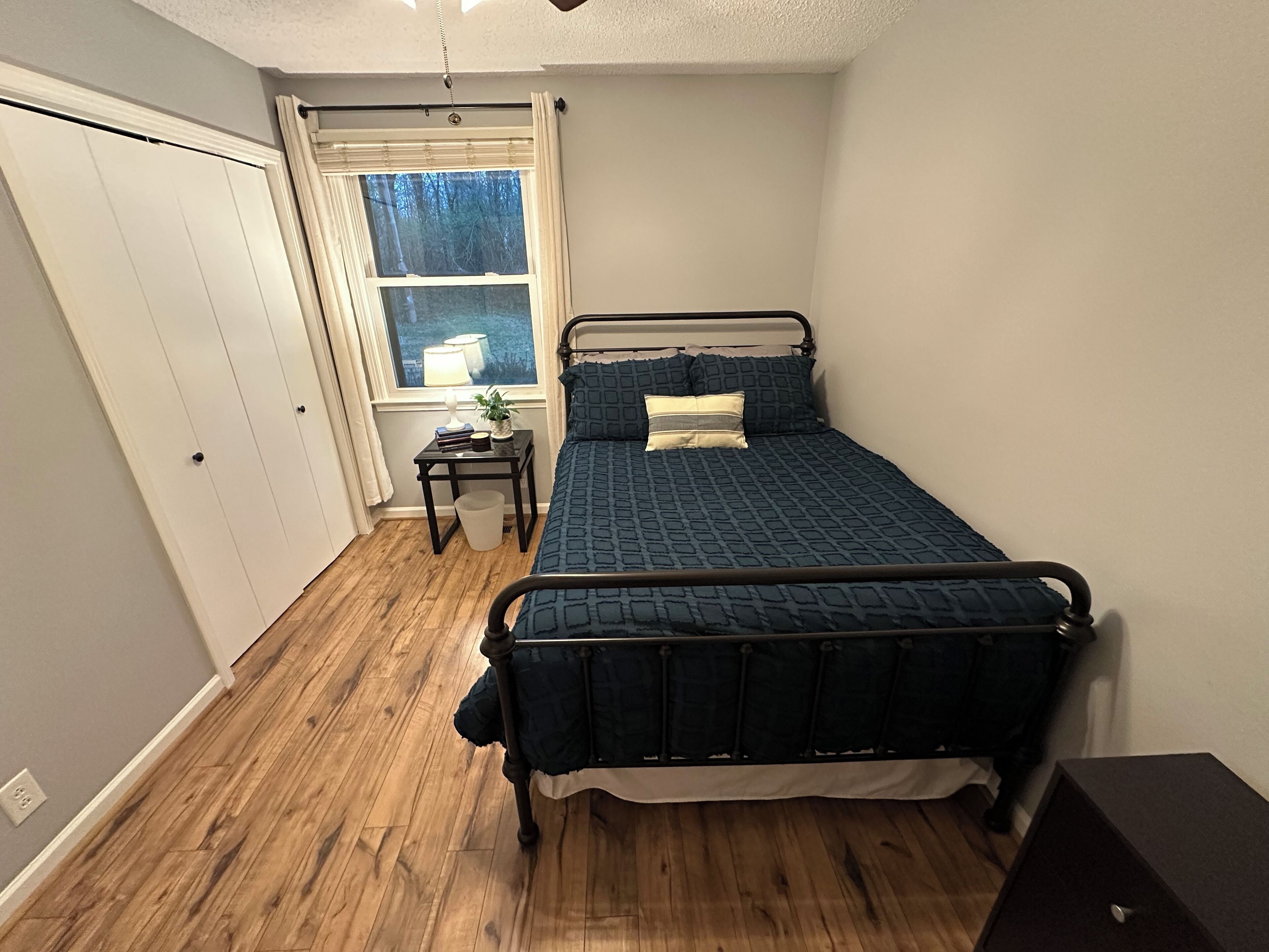 A bedroom with a bed, a nightstand, a window, and a door.