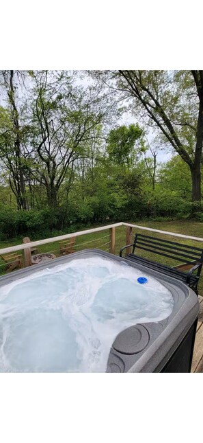 Un jacuzzi rodeado por una terraza de madera y bancos, con árboles al fondo.