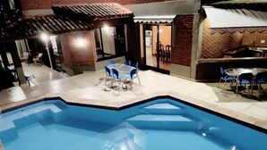 A swimming pool with blue tiles, surrounded by a patio area with chairs and tables.