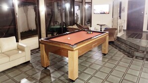 A pool table in a room with tiled flooring, a sofa, and a dining area visible through glass doors.