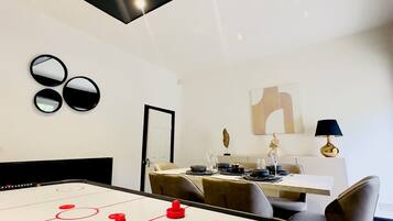 A modern dining area with a pool table, a dining table set for four, and a contemporary art piece on the wall.