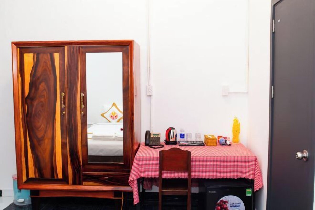 Una habitación con un armario, una pequeña mesa con mantel a cuadros rojos y varios objetos sobre la mesa, incluyendo un teléfono, una tetera y una botella.