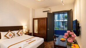Une chambre d’hôtel comprenant un lit, une table de chevet, une lampe, une armoire et un bureau agrémenté d’un vase de fleurs.