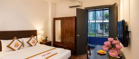 Una habitación de hotel con cama, mesita de noche, lámpara, armario y escritorio con un jarrón de flores.