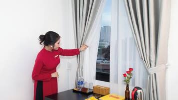 A person in a red uniform adjusting curtains in a room with a table that has a plate of food, a bottle, a basket, and a kettle.