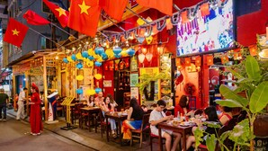 A bustling street food restaurant with outdoor seating, decorated with flags and lanterns, and a large screen displaying content. - The Rice Hotel & Tour - 131 Bui Vien (Ho Chi Minh City)